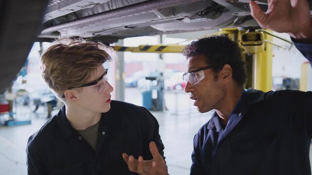 Male tutor and student looking underneath car on hydraulic ramp on auto mechanic course - shot in slow motion 