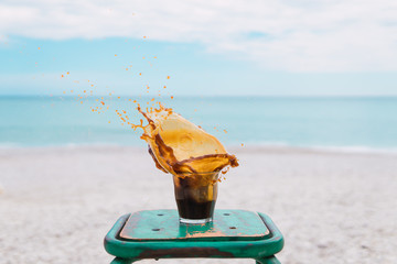 vaso transparente de cristal frente al mar azul, salpicaduras en el aire congeladas, silla verde de madera tipo vintage