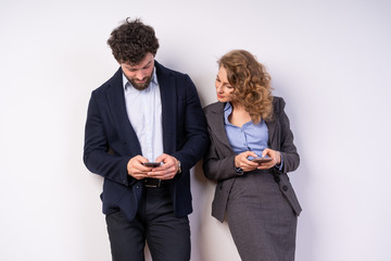 woman and man in suits, business, in a relaxed state, looking at their smartphones