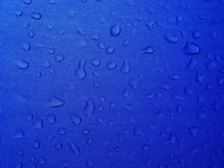 many drops of water on a blue surface. drops shine through.
