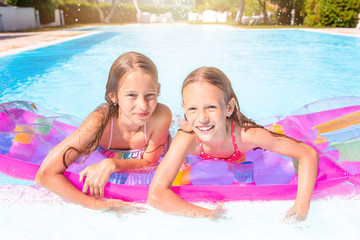 Adorable little sisters play in outdoor swimming pool