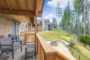 Beautiful wooden back porch with chairs on the hill and large backyard patio with fire pit and pine trees.