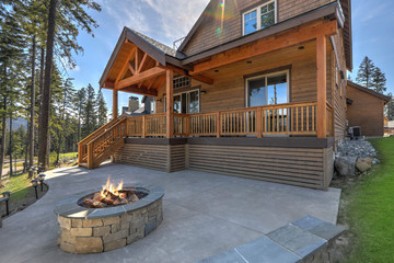 Beautiful wooden back porch with chairs on the hill and large backyard patio with fire pit and pine trees.