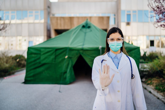 Coronavirus ER Doctor In Front Of Isolation Hospital.Covid-19 Physician With Protective Glasses / Mask Performing Triage For Virus Outbreak Patients.Hand Stop Sign.Quarantined Area.No Entrance Allowed