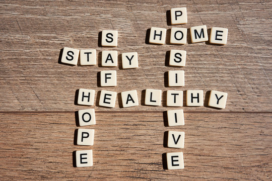 Word game with crossword grids showing various words - stay, home, hope, healthy, safe, and positive - isolated on wooden background. Stay home and be positive concept.