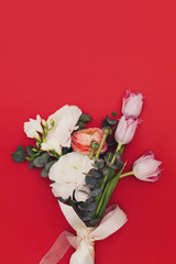 A small bride bouquet of flowers on red background with tape. Tulip, eucalyptus branches, Austin roses and ranunculus. Flat lay