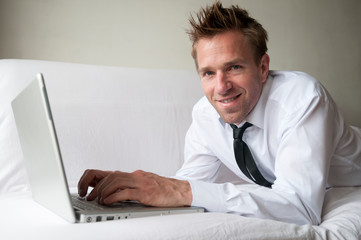 Friendly man reclining at home on comfortable white couch smiling with his laptop computer 