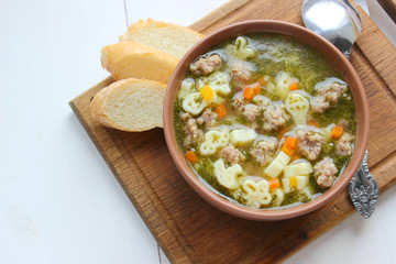 Hot soup, broth with meatballs, carrots, macaroni and fresh herbs.Delicious lunch on a wooden Board. Children's food, macaroni soup in the form of an airplane and a car.