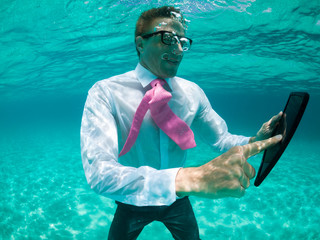 Businessman using a tablet computer standing under water in tropical turquoise sea