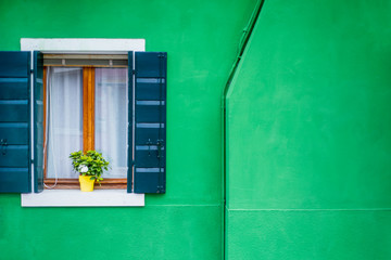 Bright green exterior of the house: wall and window with wooden shutters.