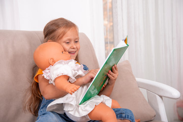 A little girl sits on the sofa   and plays with her doll or soft toy