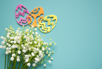 Floral blue background with fresh flowers. Spring greeting card for Easter. A bouquet of lily of the valley and a gift, eggs