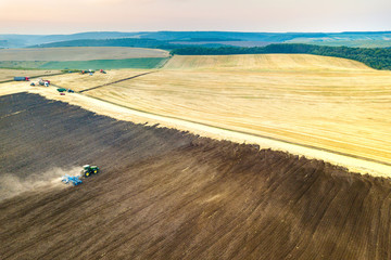 Aerial view of a tractor plowing black agriculture farm field after harvesting in late autumn.