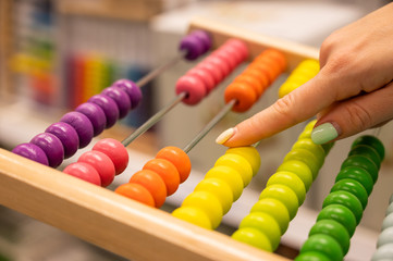 Closeup female hand calculating with balls on wooden rainbow abacus for number calculation. The concept of learning arithmetic for preschoolers.