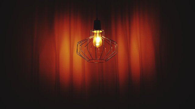 Illuminated Light Bulb Hanging Against Curtain In Dark Theater