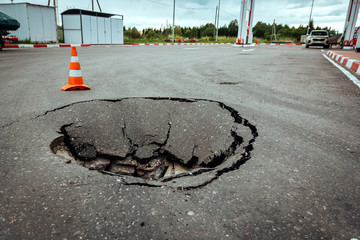 Huge Pit Sinkhole on Asphalt Road Surface and Traffic Cone restricting the movement of Cars....