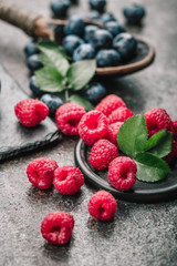 Fresh berries with raspberries, blueberries, blackberries in bowl on a stone stand on a dark metal background.