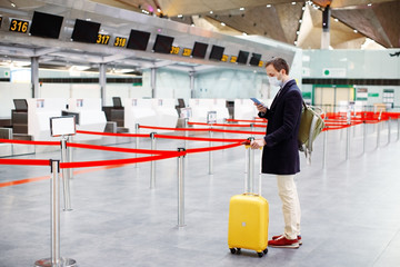 Man in mask at empty airport at check in in coronavirus quarantine isolation, returning home,...