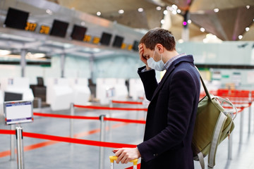 Man in mask at empty airport at check in in coronavirus quarantine isolation, waiting for departure, tourism industry crisis, pandemic infection spread, travel restrictions and border shutdown