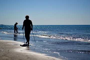 Silhouette of aged woman while Nordic walking /walking with sticks on the beach. Copy space.