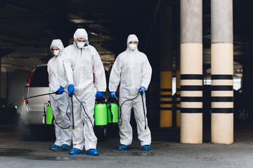 Medical workers in coronavirus hazmats holding spray bottles with disinfecting chemicals