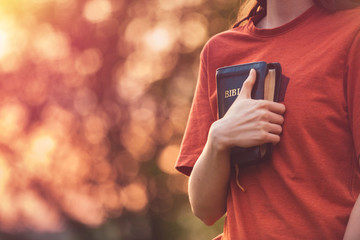 Girl holding a Bible tight as it is the only hope, beautiful warm color palette