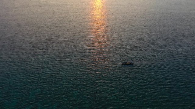 Aerial drone view of ocean with drifting fishing boat over amazing sunset reflecting on a water.