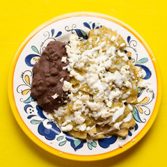 Mexican green chilaquiles with beans on yellow background