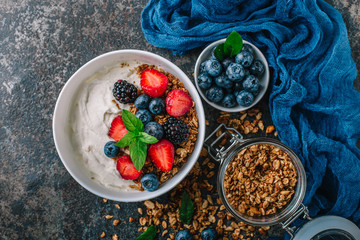 Healthy breakfast with granola, yogurt, fruits, berries on dark metal background. Summer homemade breakfast.