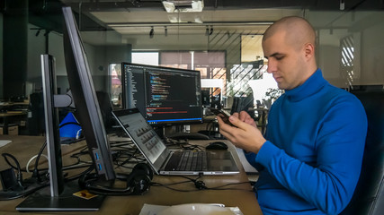 The programmer girl works at the computer and talk on phone