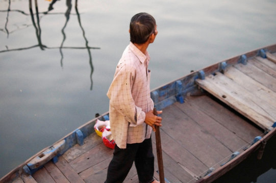 An old fisherman in a pink shirt stands in a boat