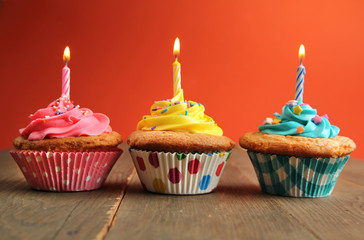 Three cupcakes with candles on orange background