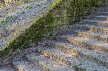 Embedded in a grassy earthen rampart, an ancient staircase consists of low, chipped steps made of gray stone blocks covered with green moss.