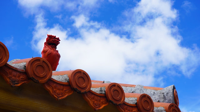 Sculpture of the mythical shisa on the roof. clay statuette on a Japanese tiled roof on background blue sky      