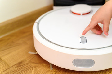 a kids hand presses the button to turn the robot vacuum cleaner on. home cleaning