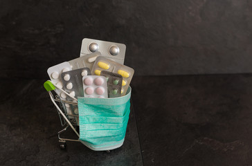 Supermarket cart for shopping with various pills on a black background. The trolley is wearing a medical mask. Corona virus control concept. Creative idea for an online pharmacy, online drug sale.