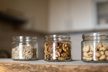 Sunflower seeds, walnut and pistachio in a jars which standing on a white vintage table with a kitchen on background. Nuts is a healthy vegetarian protein and nutritious food. Nuts on rustic old wood.