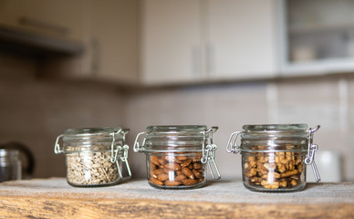 Sunflower seeds, walnut and almond in a jars which standing on a white vintage table with a kitchen on background. Nuts is a healthy vegetarian protein and nutritious food. Nuts on rustic old wood.