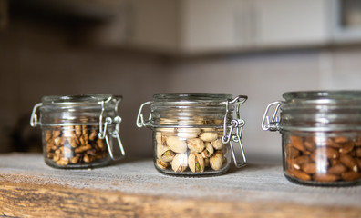 Pistachios, walnut and almond in a jars which standing on a white vintage table with a kitchen on background. Nuts is a healthy vegetarian protein and nutritious food. Nuts on rustic old wood.