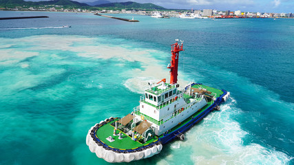 Colored tugboat works in port. bright tugboat in blue water. industrial ship on waves tropical...