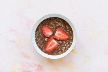Chocolate oatmeal porridge and strawberries breakfast in bowl on pink background, concept of healthy eating vegan food. Close up, selective focus, copy space
