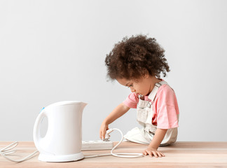 Little African-American girl playing with kettle on table. Child in danger