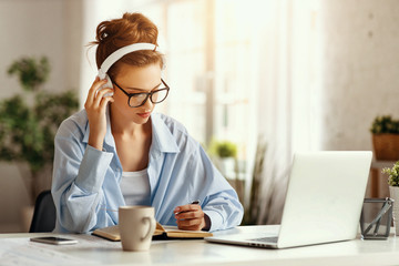 Young serious woman in headphones using laptop at home.