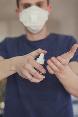 Man in medical protective mask with an antibacterial antiseptic for hands disinfection in home.