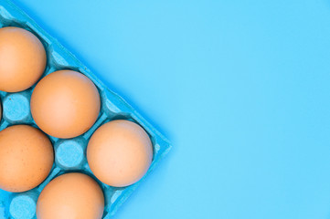 Raw brown chicken eggs on blue background .