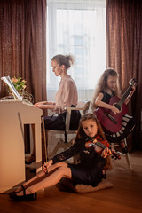 Fototapeta na wymiar Family home music group. A woman plays the piano, girls play the violin and the guitar. Quarantine homework