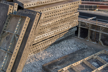 Stacked in a high stack black metal frame plates for foundation works with perforated round holes. Next to it is a mounted structure for pouring cement at a road junction with tram rails.