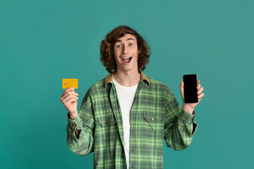 Online shopping. Happy guy holding smartphone with blank screen and credit card on color background. Space for design