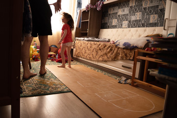 Child playing hopscotch with dad inside at her home healthy body lifestyle concept, side view. what to do in quarantine. street entertainment in the house during self-isolation