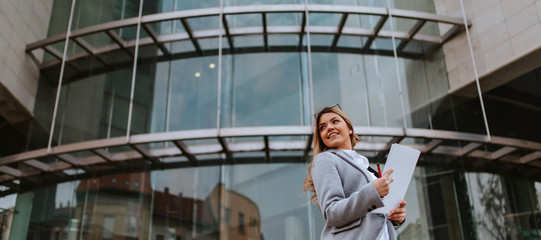 Young attractive caucasian businesswoman with notebook in front of company